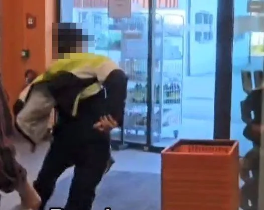 Ein junger Mann mit gelb-schwarzer Jacke und schwarzer Baseball-Mütze rennt aus einem Migros-Laden.